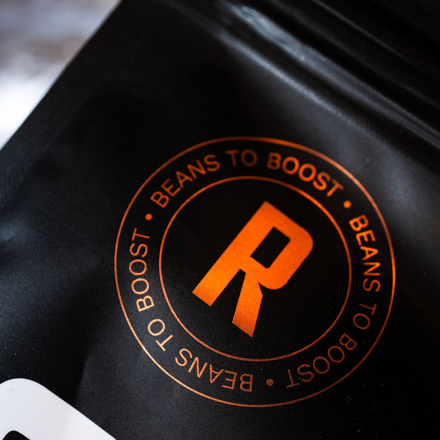 Detailaufnahme des Robooster Logos auf schwarzer Kaffeeverpackung.