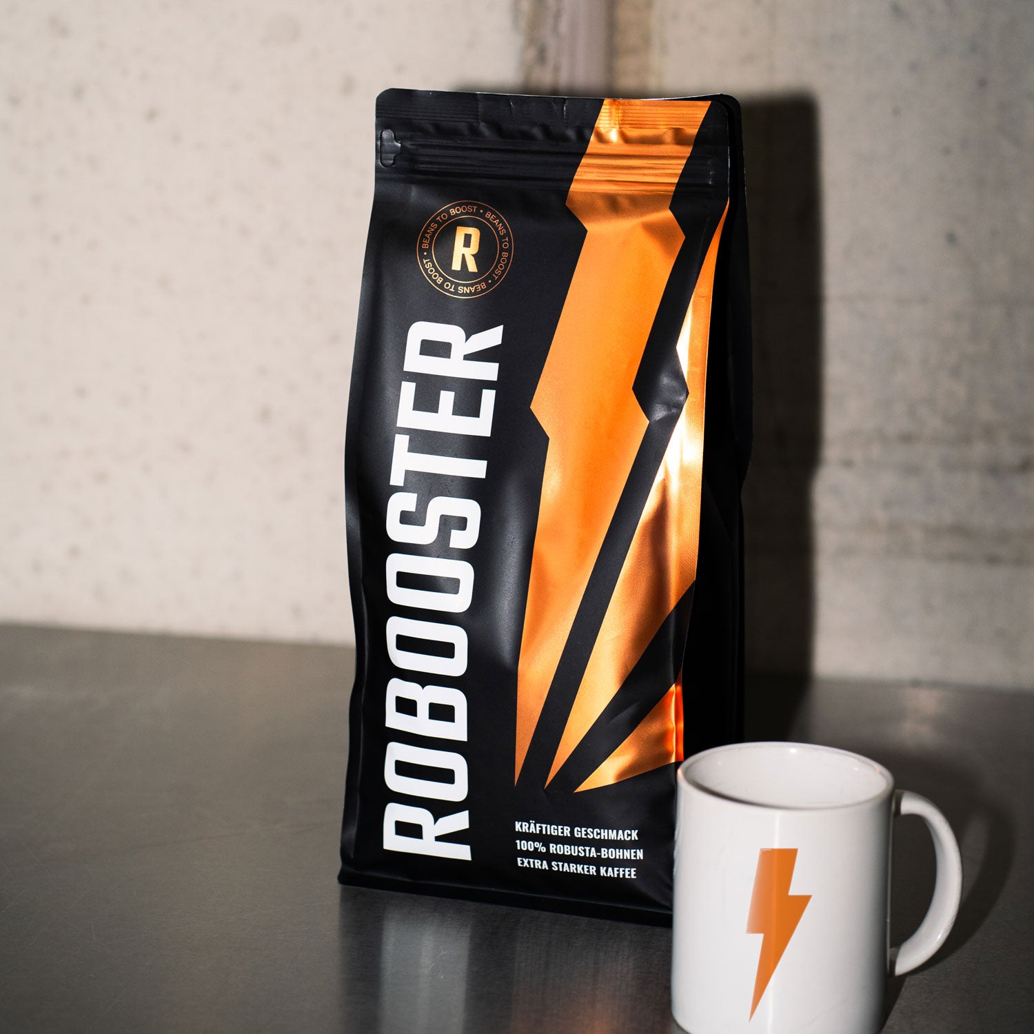 Robooster Kaffee Packung stehend auf hellem Untergrund mit einer Tasse.